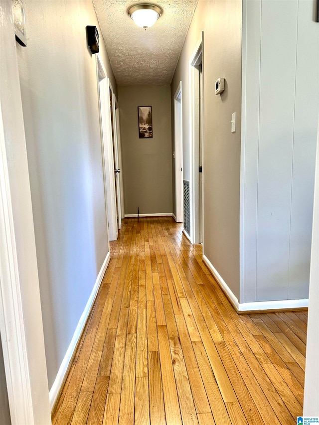 hallway with light wood-type flooring and a textured ceiling