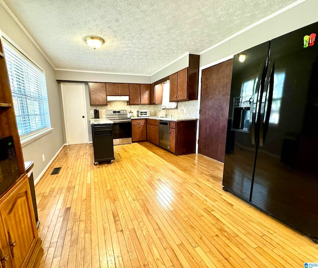 kitchen with decorative backsplash, appliances with stainless steel finishes, ornamental molding, sink, and light hardwood / wood-style flooring