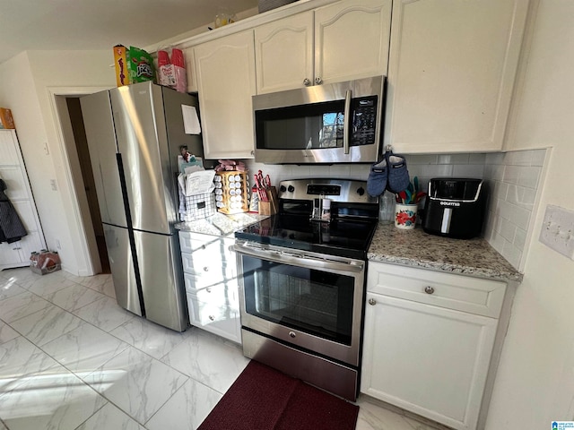 kitchen featuring light stone counters, white cabinetry, appliances with stainless steel finishes, and tasteful backsplash