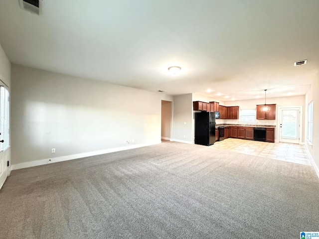 unfurnished living room with sink, carpet floors, and a healthy amount of sunlight