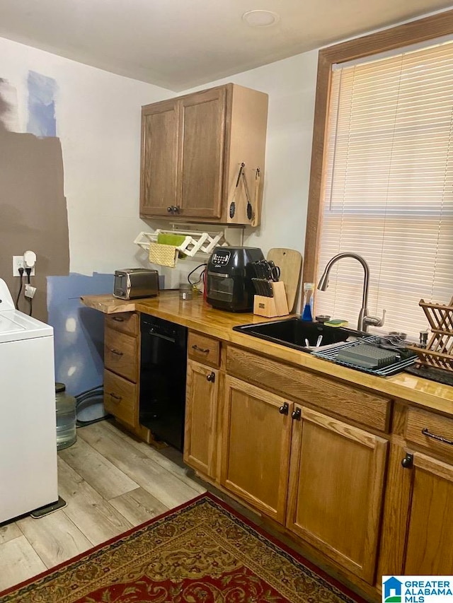 kitchen with black dishwasher, washer / dryer, light wood-type flooring, and sink