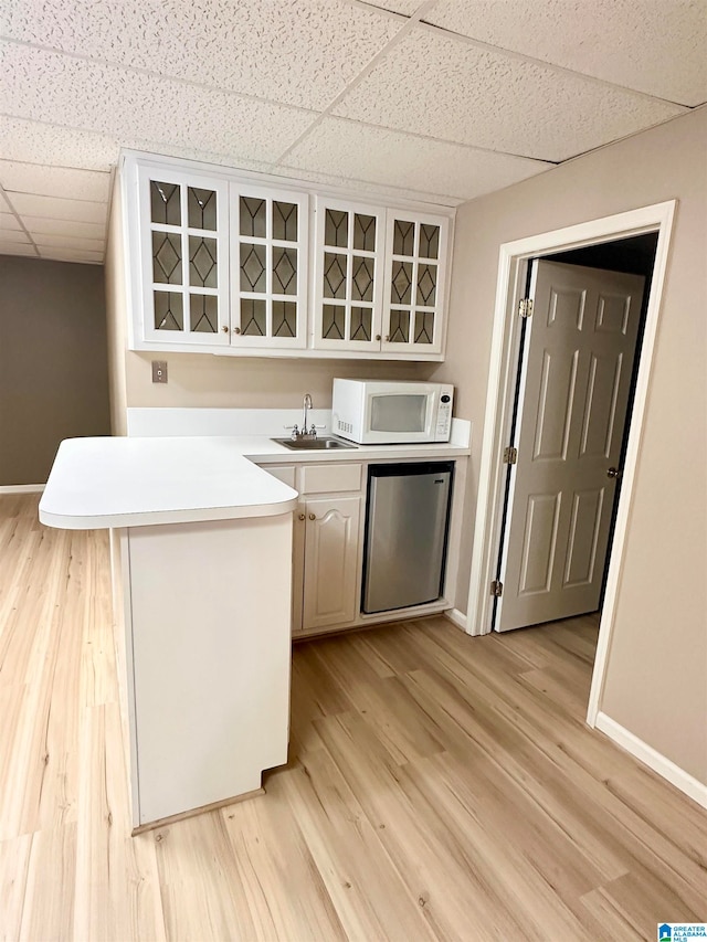 kitchen featuring stainless steel fridge, kitchen peninsula, a paneled ceiling, and light wood-type flooring