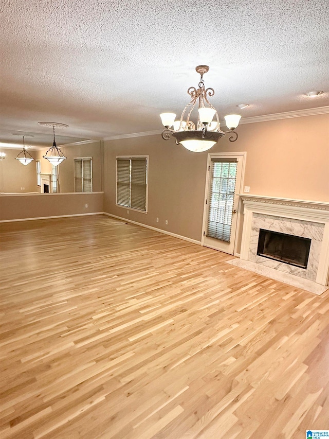 unfurnished living room featuring a premium fireplace, light hardwood / wood-style floors, a textured ceiling, and an inviting chandelier