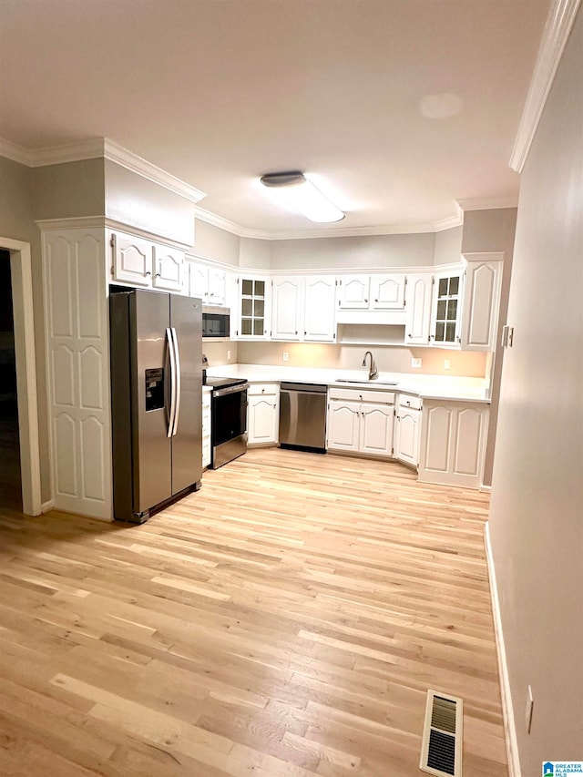 kitchen featuring white cabinetry, light hardwood / wood-style flooring, ornamental molding, and appliances with stainless steel finishes