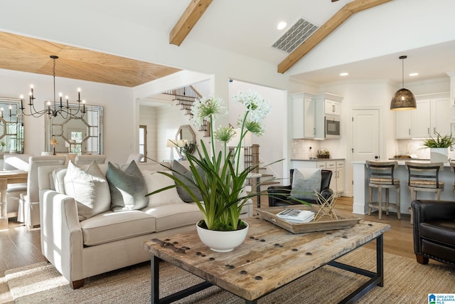 living room with beamed ceiling, an inviting chandelier, high vaulted ceiling, and light wood-type flooring