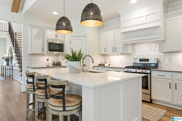 kitchen featuring stainless steel appliances, sink, decorative light fixtures, white cabinets, and an island with sink