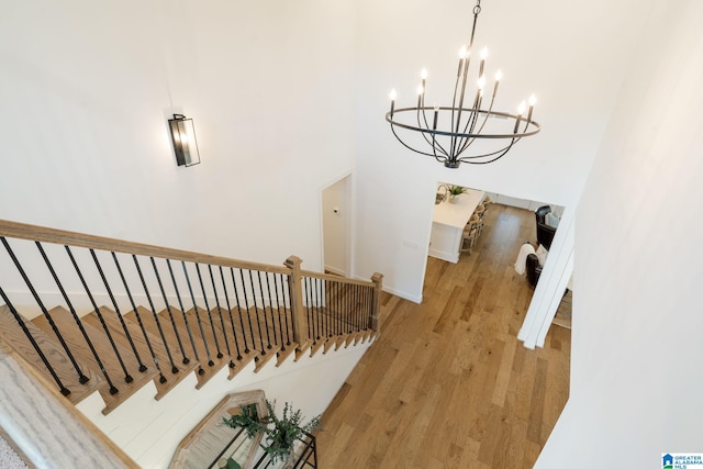 stairs with a notable chandelier, wood-type flooring, and a towering ceiling