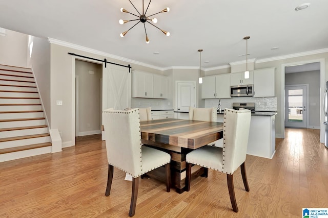 dining space with sink, an inviting chandelier, a barn door, light hardwood / wood-style flooring, and crown molding