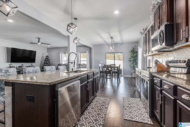 kitchen featuring sink, stainless steel appliances, dark wood-type flooring, pendant lighting, and a kitchen island with sink