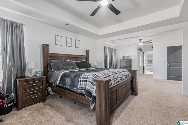 bedroom featuring light carpet, a tray ceiling, and ceiling fan