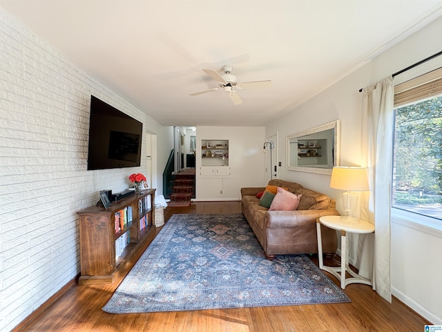 living room with ceiling fan, dark hardwood / wood-style flooring, and brick wall