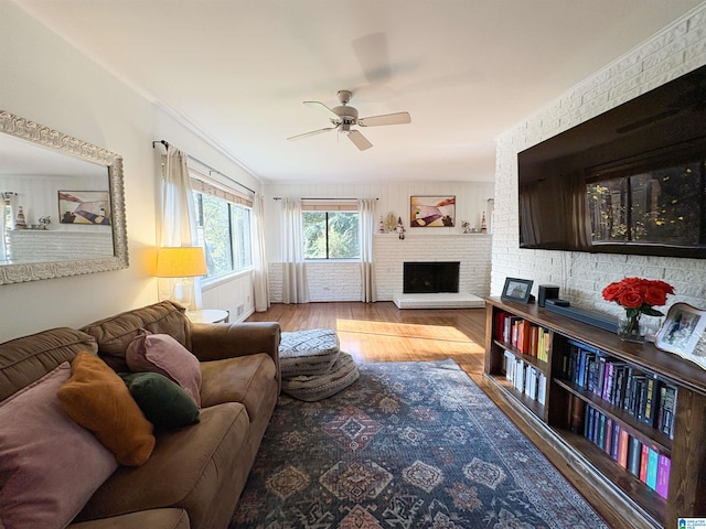 living room with ceiling fan, a brick fireplace, brick wall, crown molding, and light hardwood / wood-style floors