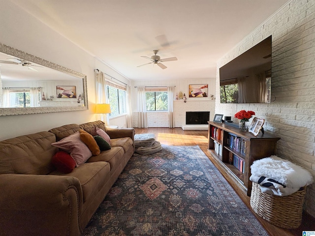 living room featuring hardwood / wood-style flooring, ceiling fan, a fireplace, and brick wall