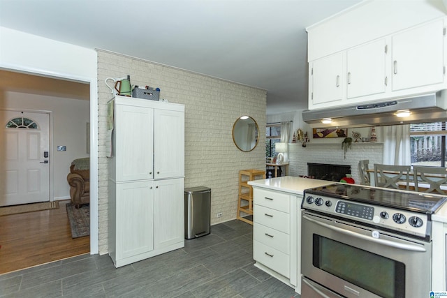 kitchen featuring dark hardwood / wood-style floors, white cabinets, brick wall, and stainless steel range with electric stovetop