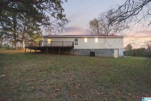 back house at dusk featuring a deck, cooling unit, and a lawn