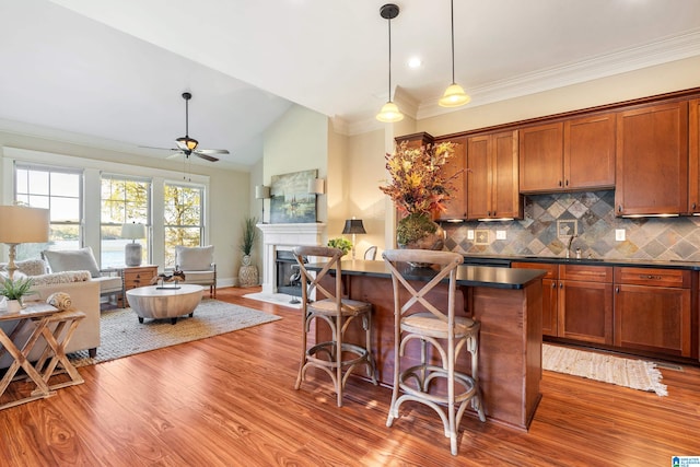 kitchen with ceiling fan, a kitchen breakfast bar, backsplash, wood-type flooring, and lofted ceiling