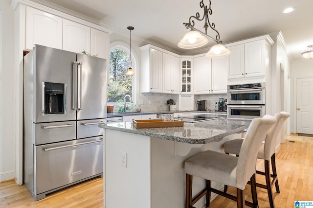 kitchen with appliances with stainless steel finishes, light wood-type flooring, white cabinetry, and dark stone countertops