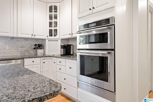 kitchen with stainless steel appliances, backsplash, dark stone countertops, light hardwood / wood-style floors, and white cabinets