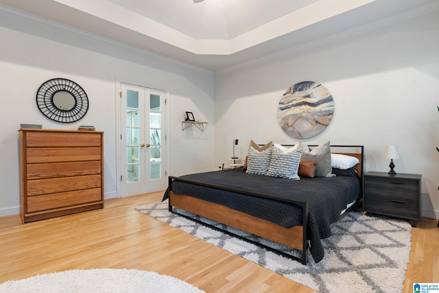 bedroom with french doors, a tray ceiling, access to outside, hardwood / wood-style flooring, and ornamental molding