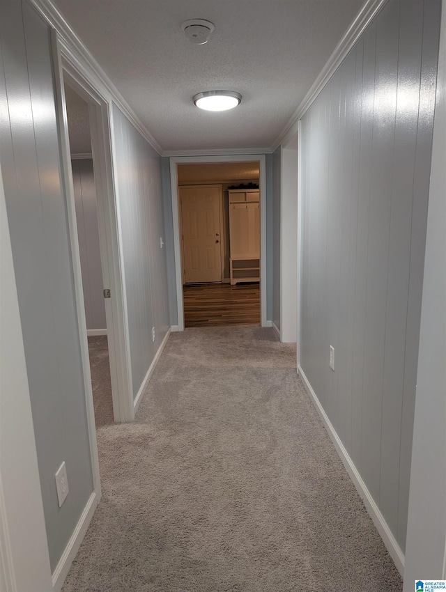 hallway with a textured ceiling, crown molding, and light carpet