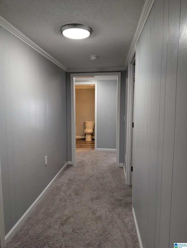 hallway with a textured ceiling, ornamental molding, and light carpet