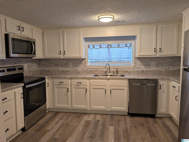 kitchen with sink, hardwood / wood-style flooring, appliances with stainless steel finishes, tasteful backsplash, and white cabinetry