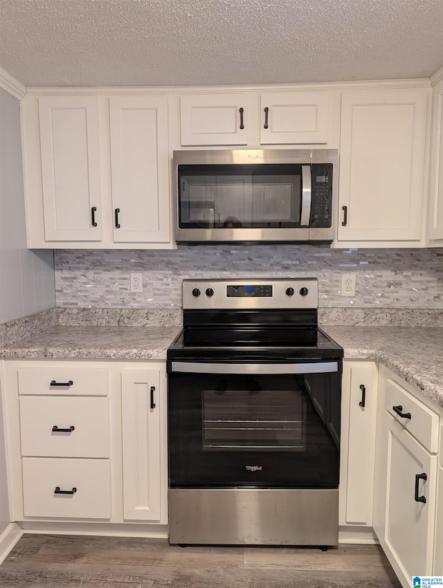 kitchen with hardwood / wood-style flooring, decorative backsplash, white cabinetry, and appliances with stainless steel finishes