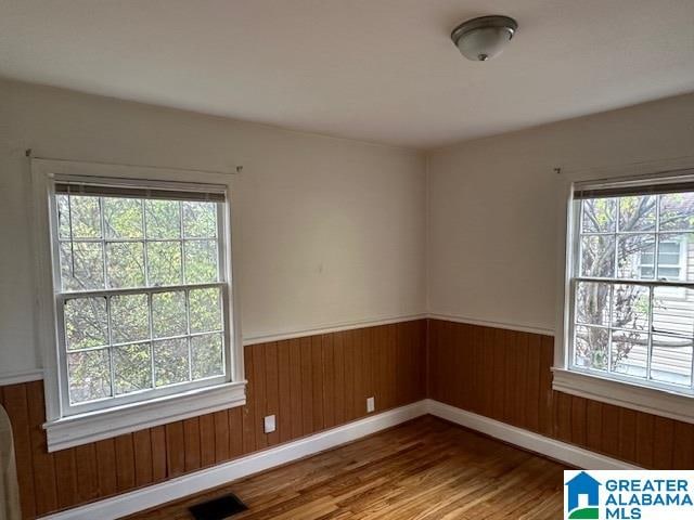 unfurnished room featuring wood-type flooring, a wealth of natural light, and wood walls