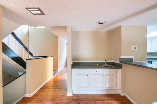 kitchen featuring a textured ceiling, light wood-type flooring, white cabinetry, and sink