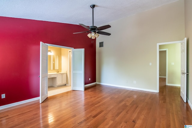 unfurnished bedroom with ensuite bath, a high ceiling, a textured ceiling, ceiling fan, and hardwood / wood-style floors