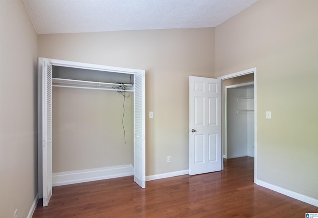 unfurnished bedroom featuring a textured ceiling, lofted ceiling, a closet, and dark wood-type flooring