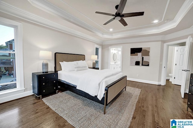 bedroom with crown molding, ceiling fan, connected bathroom, a tray ceiling, and dark hardwood / wood-style flooring