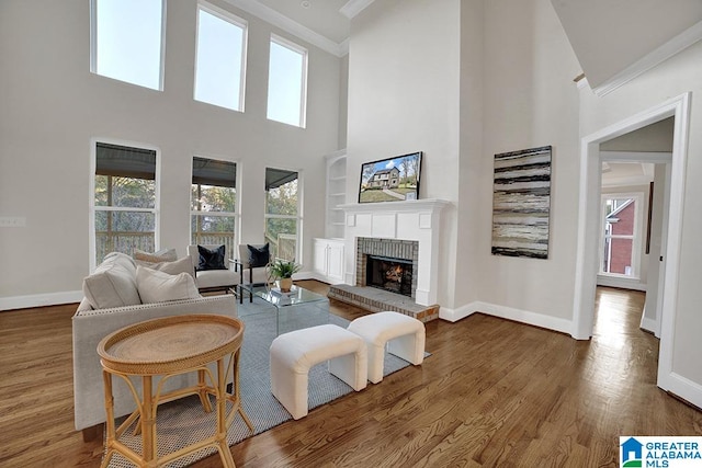 living room featuring crown molding, hardwood / wood-style floors, a high ceiling, and a brick fireplace