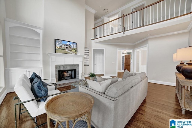 living room featuring hardwood / wood-style floors, a fireplace, a towering ceiling, and crown molding