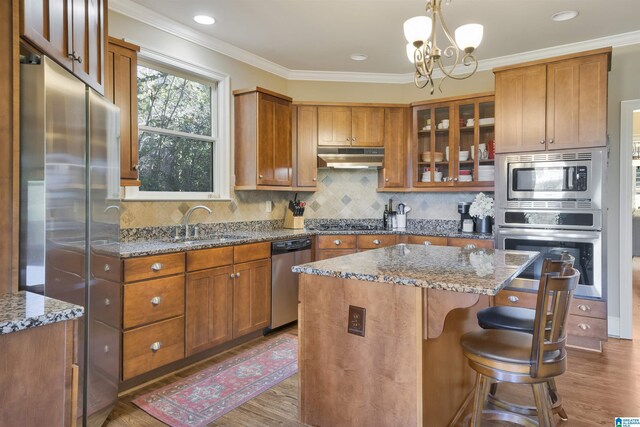 2399 Huntington Glen Dr, Homewood, AL 35226 - kitchen featuring stainless steel appliances, wood finished floors, a sink, under cabinet range hood, and crown molding