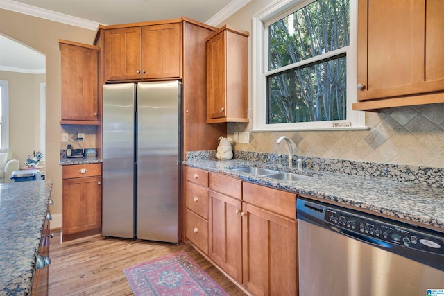 kitchen featuring light wood-type flooring, stainless steel appliances, crown molding, sink, and stone counters