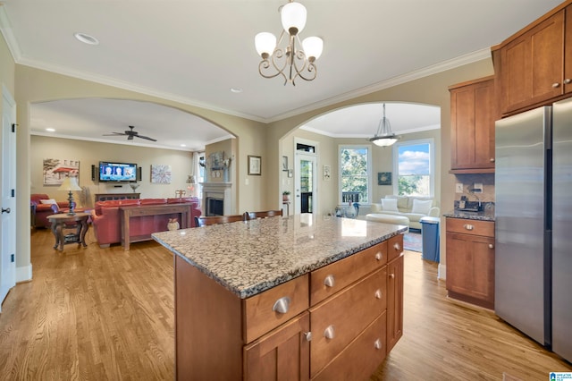 kitchen with stainless steel fridge, ceiling fan with notable chandelier, decorative light fixtures, light hardwood / wood-style flooring, and a kitchen island