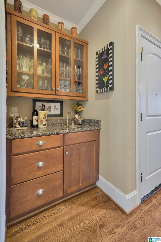 bar with sink, dark stone countertops, light wood-type flooring, and ornamental molding