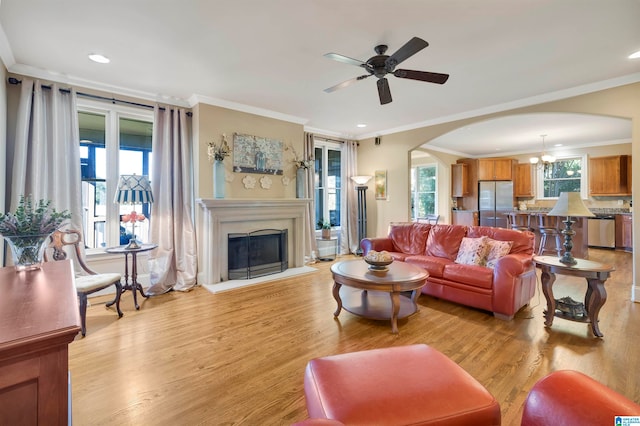 living room featuring ceiling fan with notable chandelier, ornamental molding, and light hardwood / wood-style flooring