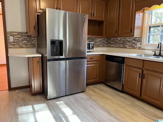 kitchen with decorative backsplash, stainless steel appliances, light hardwood / wood-style floors, and sink