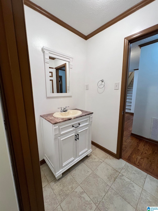 bathroom with a textured ceiling, vanity, crown molding, and wood-type flooring