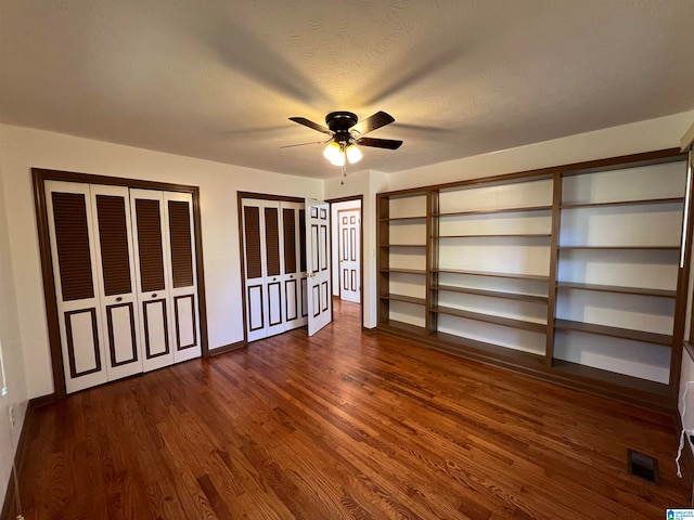 unfurnished bedroom with a textured ceiling, dark hardwood / wood-style flooring, ceiling fan, and multiple closets