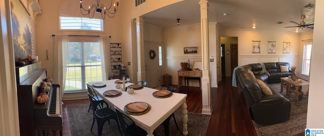 dining area with a towering ceiling, ornate columns, ceiling fan with notable chandelier, crown molding, and dark hardwood / wood-style floors