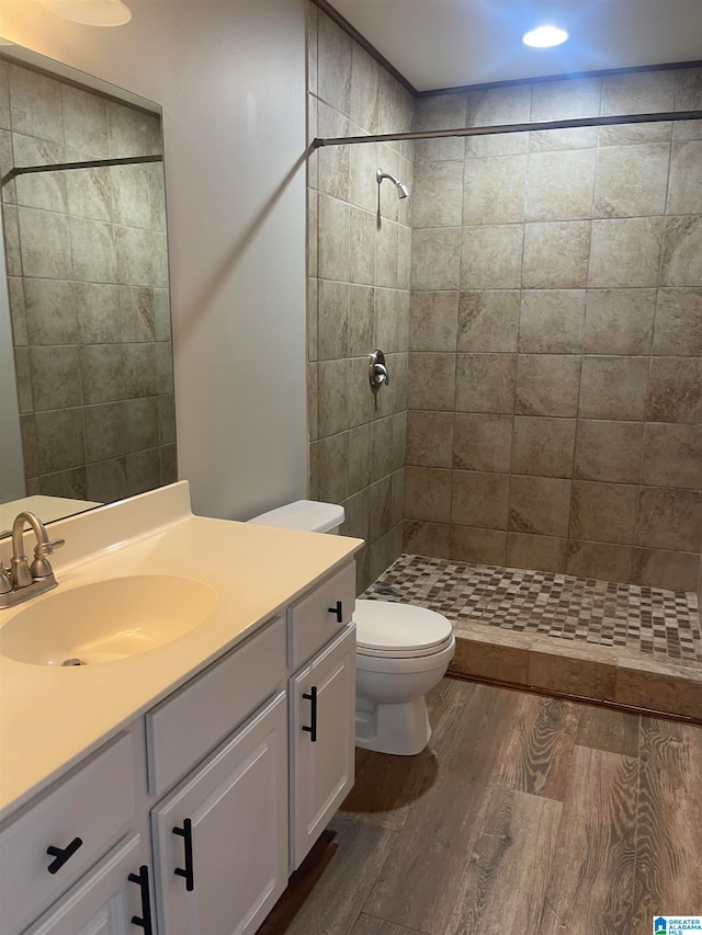 bathroom with a tile shower, hardwood / wood-style flooring, vanity, and toilet