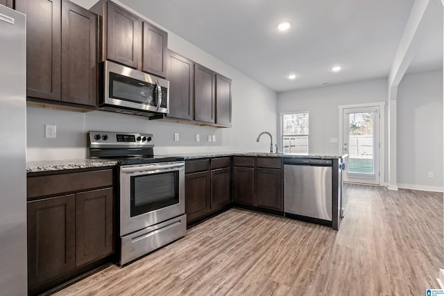 kitchen featuring kitchen peninsula, appliances with stainless steel finishes, light hardwood / wood-style floors, and light stone counters