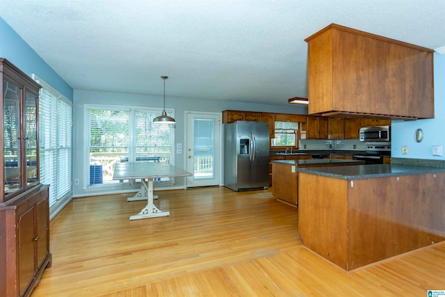 kitchen with hanging light fixtures, stainless steel appliances, a textured ceiling, and light wood-type flooring