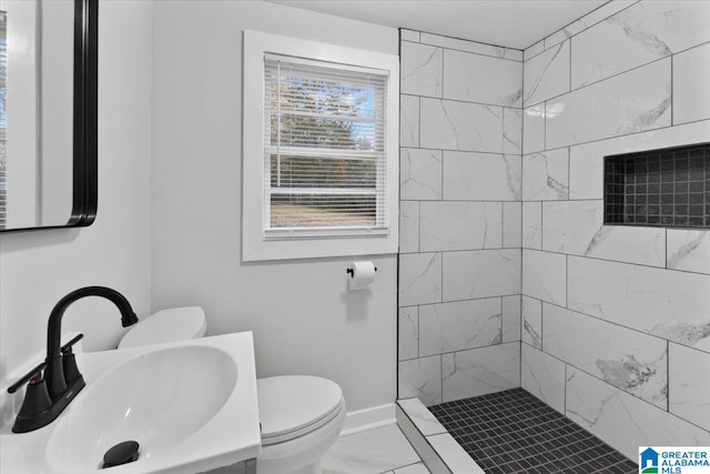 bathroom with a tile shower, sink, and toilet