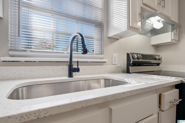 kitchen with light stone countertops, white cabinets, stainless steel range with electric cooktop, and sink