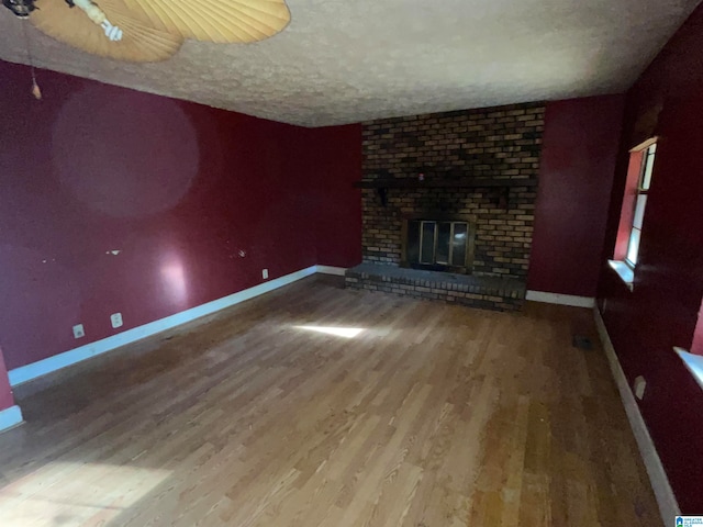 unfurnished living room with hardwood / wood-style floors, a textured ceiling, and a brick fireplace