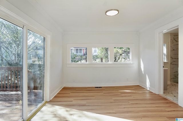 empty room featuring light wood-type flooring, a wealth of natural light, and crown molding